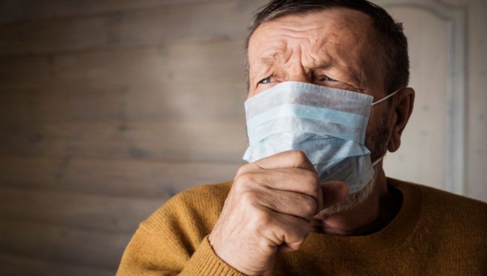 elderly man in medical mask coughs at home