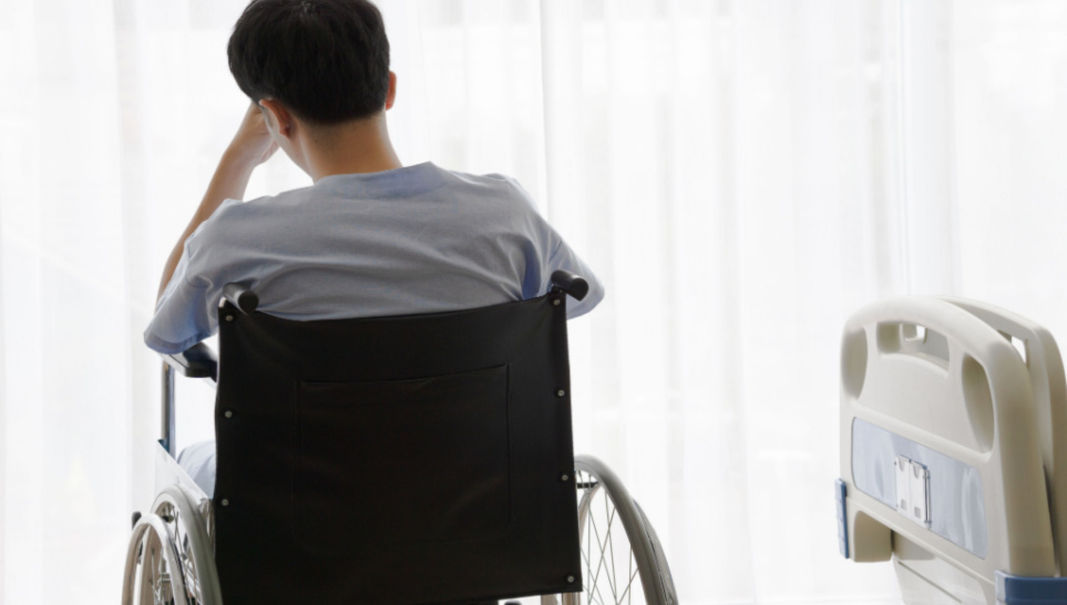 young male patient sits on wheelchair due to muscle severe weakness after getting vaccination
