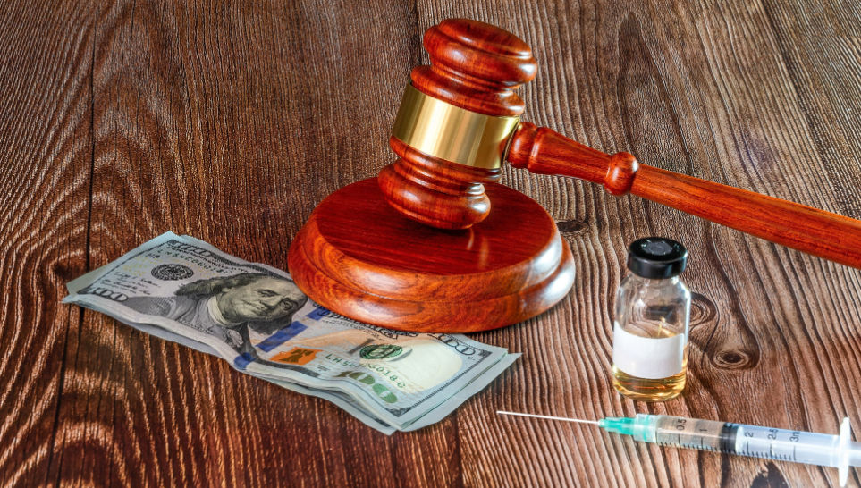 gavel dollar notes syringe and vaccine bottle on a wooden background