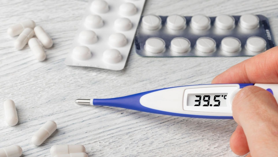 hand holding thermometer with a high temperature with pills and capsules